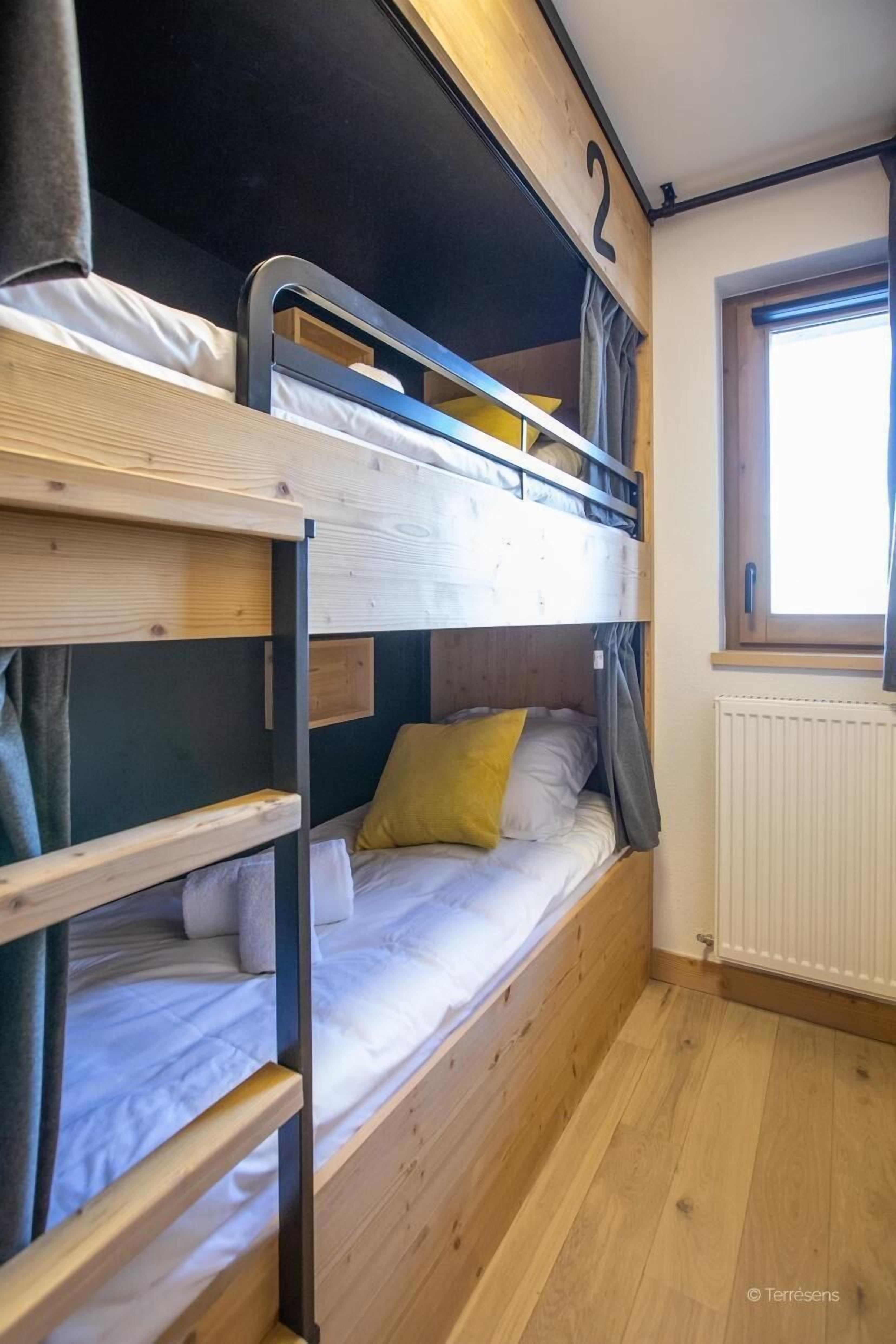 A bunk bed room with a window, wooden flooring, and a radiator.