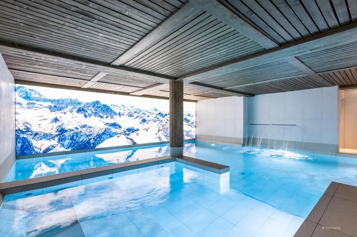An indoor swimming pool with a view of snow-capped mountains.