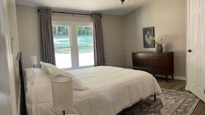 Une chambre à coucher comprenant un lit, une table de chevet, une commode, un tapis et une fenêtre avec des rideaux.