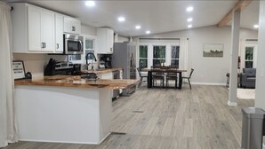 Une cuisine moderne avec des meubles blancs, un plan de travail en bois et un coin repas comprenant une table et des chaises.