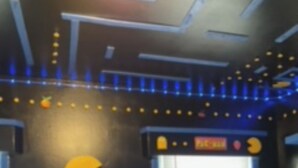 A room with a Pac-Man themed wall, a window with blinds, and a small table with a ghost decoration.