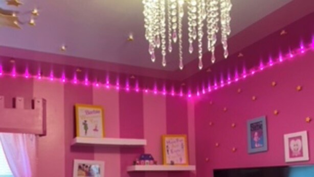 A room with pink walls, a chandelier, and a flat-screen TV mounted on the wall.