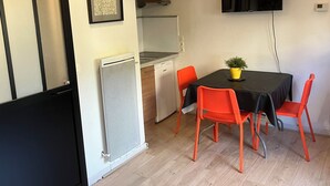 A compact kitchen with a microwave, a small refrigerator, and a sink. There is a dining table with four orange chairs and a potted plant on it. A flat-screen TV is mounted on the wall above the table. - Le Merle Rose, house with garden, quiet and close to the center (Toulouse)