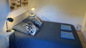 A bedroom with a bed, two pillows, a bedside lamp, a wall-mounted light, and a power outlet. - Le Merle Rose, house with garden, quiet and close to the center (Toulouse)