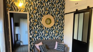 A room with a grey sofa, patterned wallpaper, a wooden floor, and a black sliding door. - Le Merle Rose, house with garden, quiet and close to the center (Toulouse)