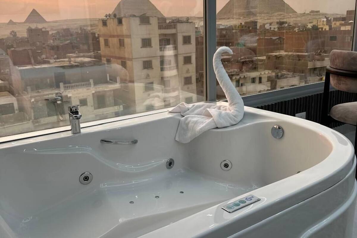 Ein modernes Badezimmer mit einer großen Badewanne, einer badematte in Schwanenform und Blick auf Pyramiden durch ein großes Fenster.