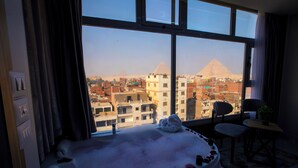 A room with a bathtub filled with water and rose petals, a view of the pyramids, and a small table with a plant. - Royal Pyramids View Inn (Giza)