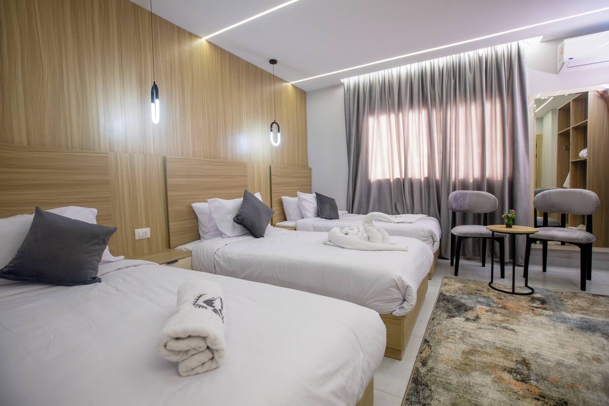 Ein Hotelzimmer mit zwei Betten, einem kleinen Tisch, einem Sessel und einem großen Fenster mit Vorhängen.