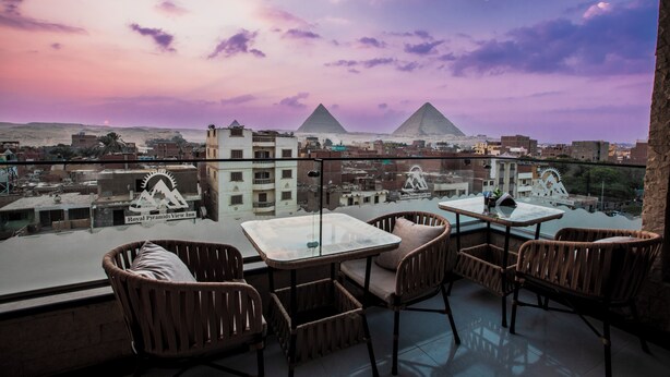 A balcony with wicker chairs and a glass table overlooking the pyramids. - Royal Pyramids View Inn (Giza)