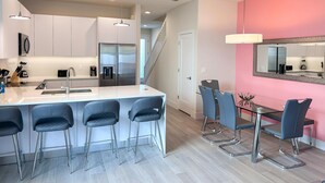 A modern kitchen with a central island, stainless steel appliances, and a dining area with bar stools and a glass table.