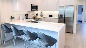 A modern kitchen with white cabinetry, stainless steel appliances, and a central island with bar stools.