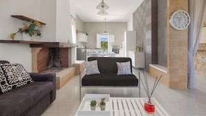 Ein modernes Wohnzimmer mit Kamin, einer Couch, einem Couchtisch mit Pflanzen und einer Küche im Hintergrund.