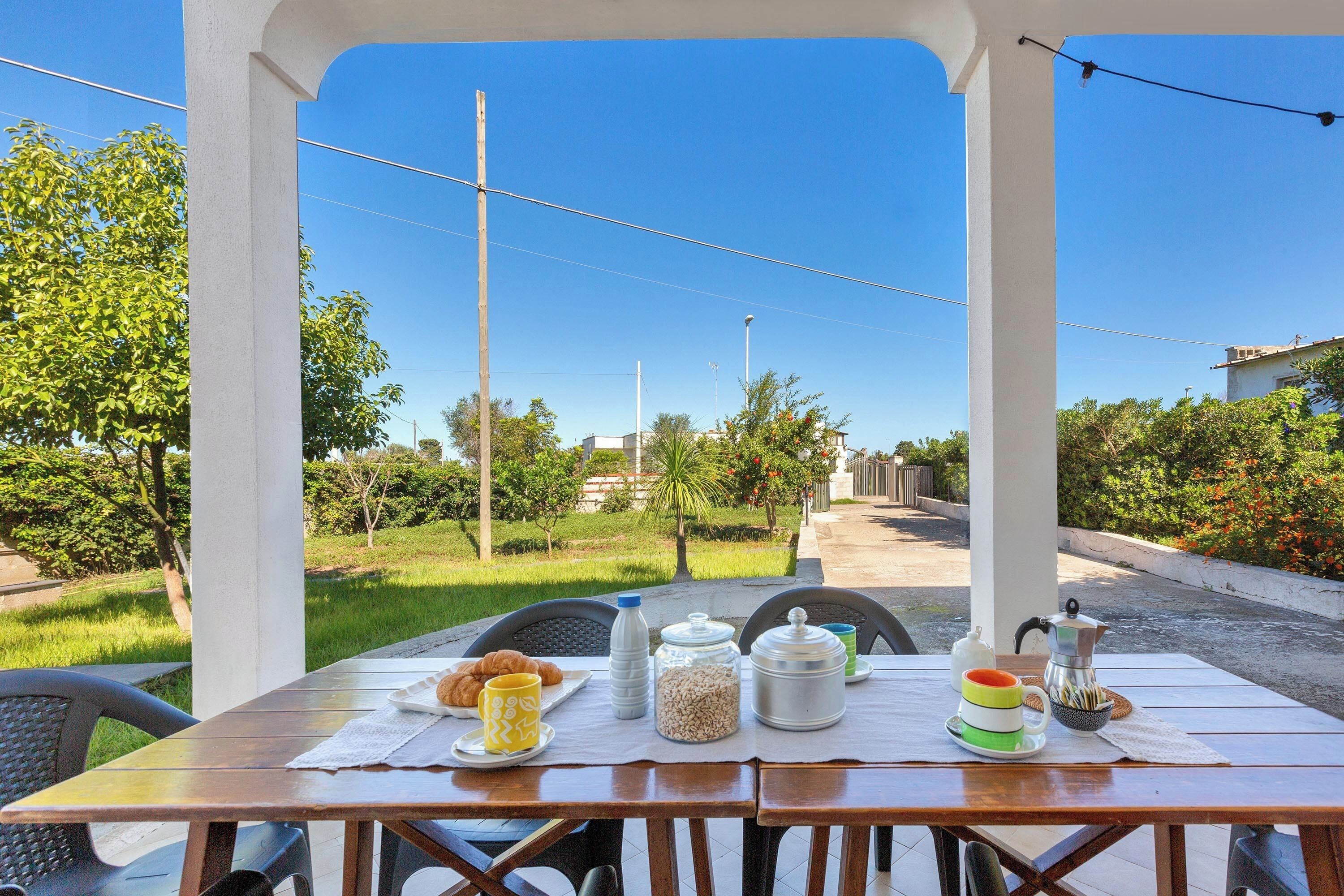 An outdoor dining area with a table set for breakfast, including croissants, coffee, and condiments.
