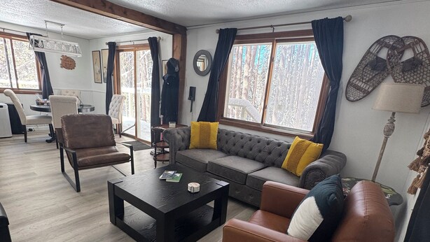 Un salon spacieux comprenant un canapé, des fauteuils et une table basse. On y trouve également un coin repas avec une table et des chaises, ainsi que de grandes fenêtres dotées de rideaux.