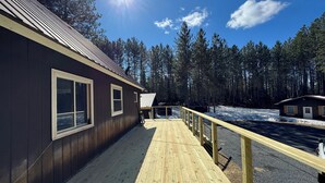 Une terrasse en bois menant à un chalet doté d’un toit en métal, le tout entouré d’une forêt.