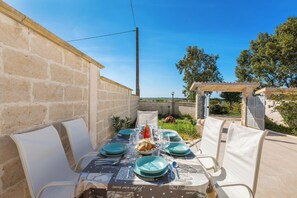 An outdoor dining area with a table set for four, surrounded by stone walls and a pergola. - Villa I Doni della Luna by BarbarHouse (Porto Cesareo)