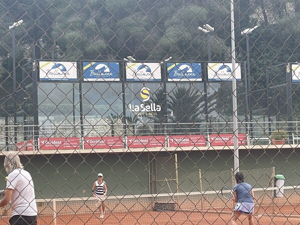 Cancha de tenis con publicidad, una valla y una pelota en juego.