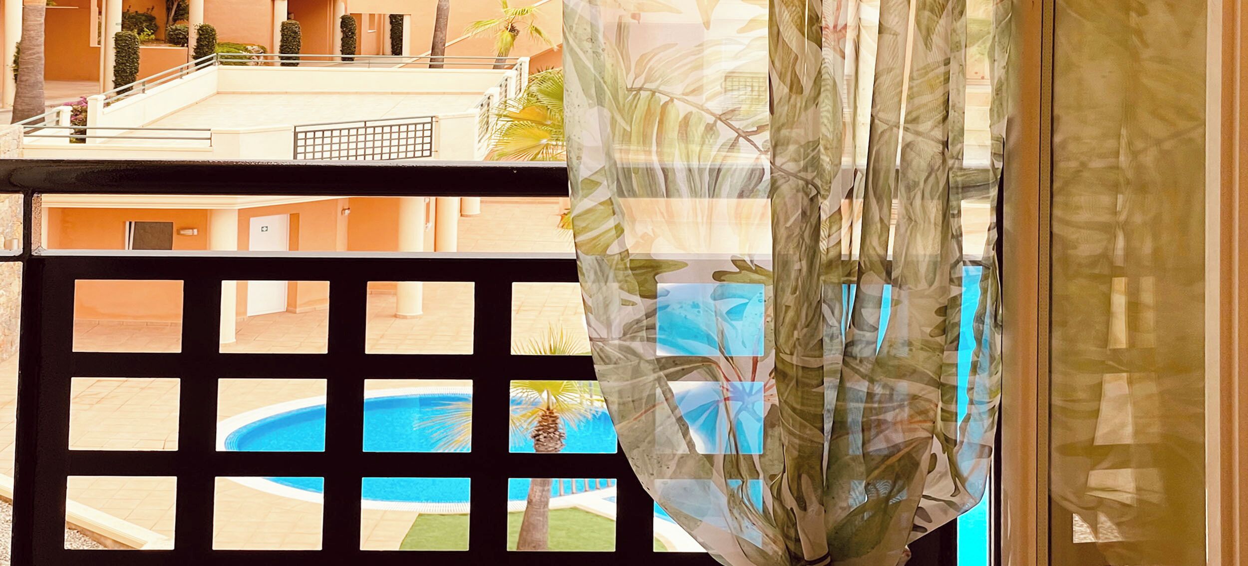 Vista attraverso una finestra con un motivo a griglia nera, una piscina e un edificio con tetto piatto e palme.