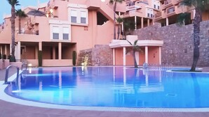 Une piscine entourée d’un mur de pierre et un bâtiment doté de balcons.