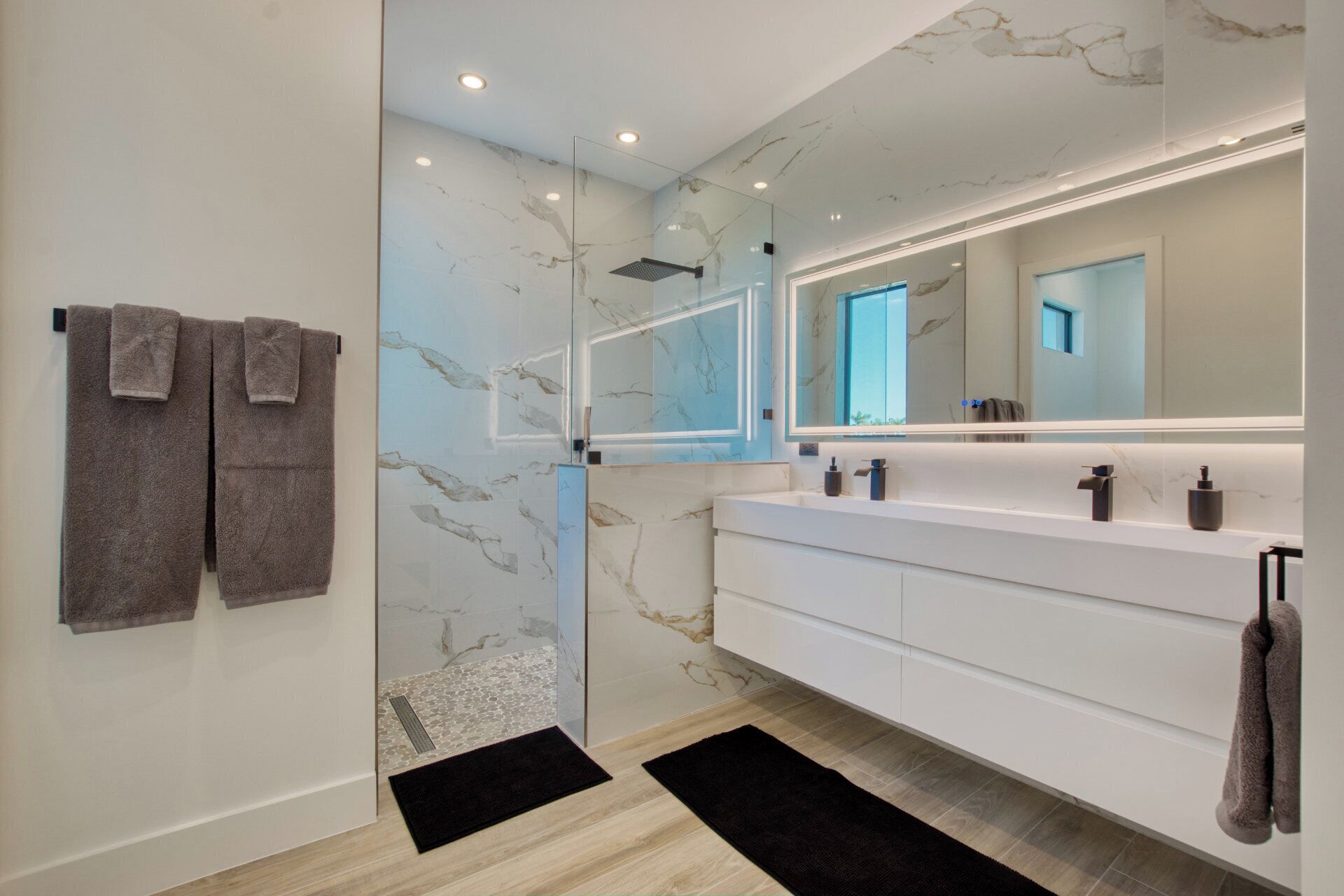 Un baño moderno con cabina de ducha de vidrio, paredes de mármol y un espejo grande.