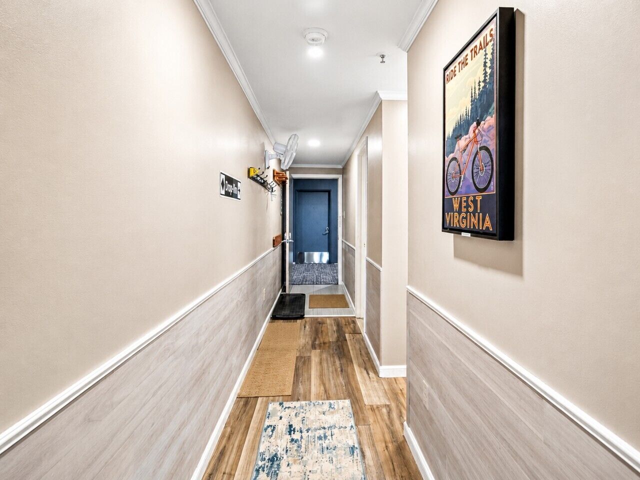 A hallway with wooden flooring, a blue door at the end, and a poster on the wall.