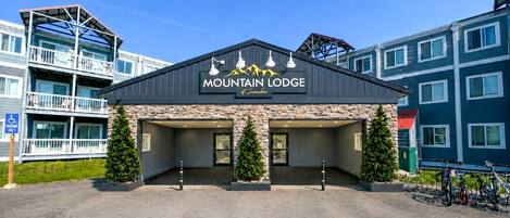 A building labeled 'Mountain Lodge' with a stone facade, two entrance doors, and a parking area with bicycles.
