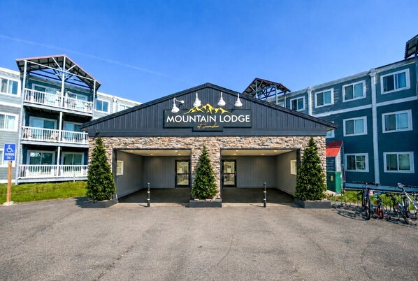A building labeled 'Mountain Lodge' with a stone facade, two entrance doors, and a parking area with bicycles.