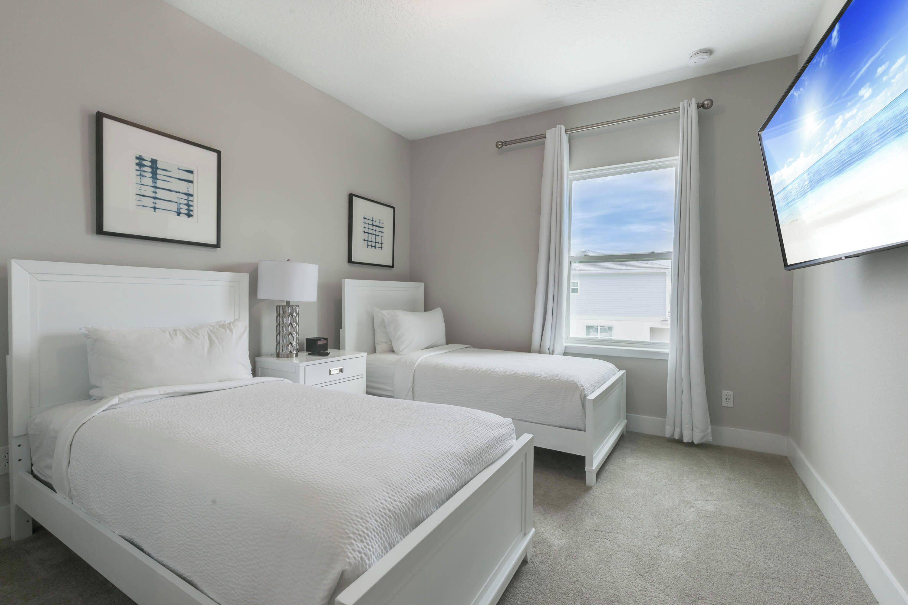 A hotel room with two beds, a large window with curtains, and a flat-screen TV mounted on the wall.