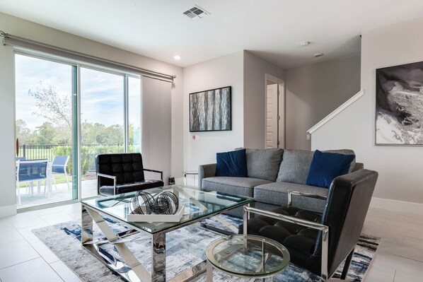 A modern living room with a glass coffee table, grey sofa, and black leather armchair. - RR796DRC - Perfect Getaway in Reunion for up to 6 guest (Kissimmee)