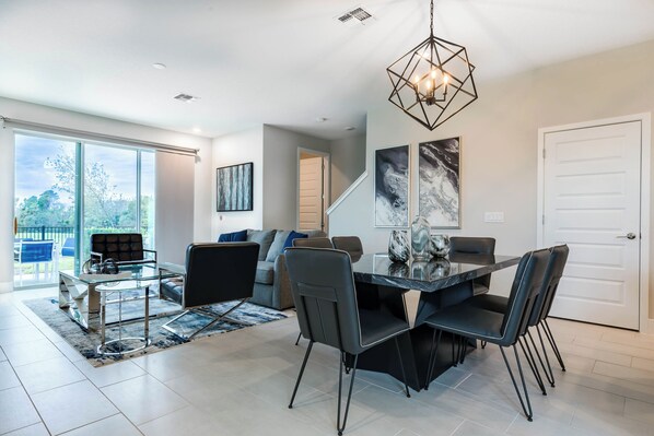 A modern living room with a glass dining table, black chairs, a sofa, and a staircase leading to another level.
