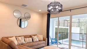 Un salon moderne avec un canapé d’angle marron, une table basse en bois et une grande porte-fenêtre coulissante donnant sur un balcon avec une piscine.