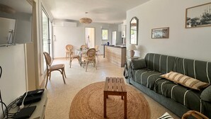 Una sala de estar moderna con un sofá verde, una mesa de centro de madera y un comedor con sillas de mimbre.