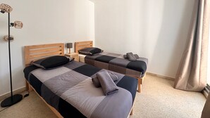 Una habitación de hotel con dos camas, una mesita de noche con lámpara, y una lámpara de pie.
