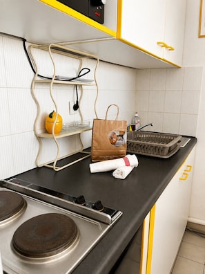 A kitchen with a stove, a coffee machine, a kettle, a bag of groceries, and a tray of dishes.