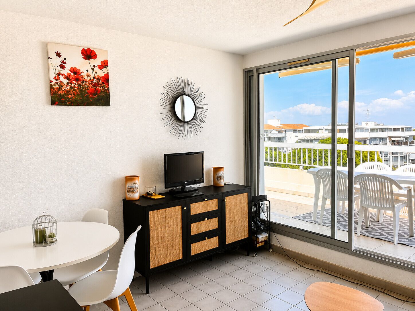 A modern living room with a TV, a decorative mirror, and a painting of flowers.