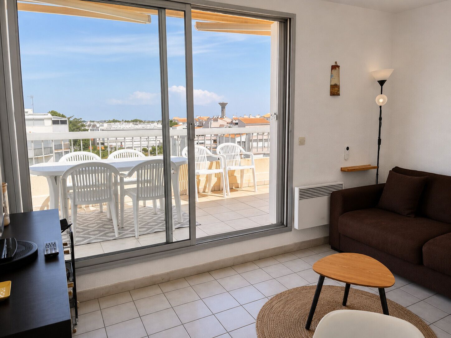 Une pièce dotée d’une grande porte-fenêtre coulissante donnant sur une terrasse extérieure avec des chaises et une table en plastique blanc.