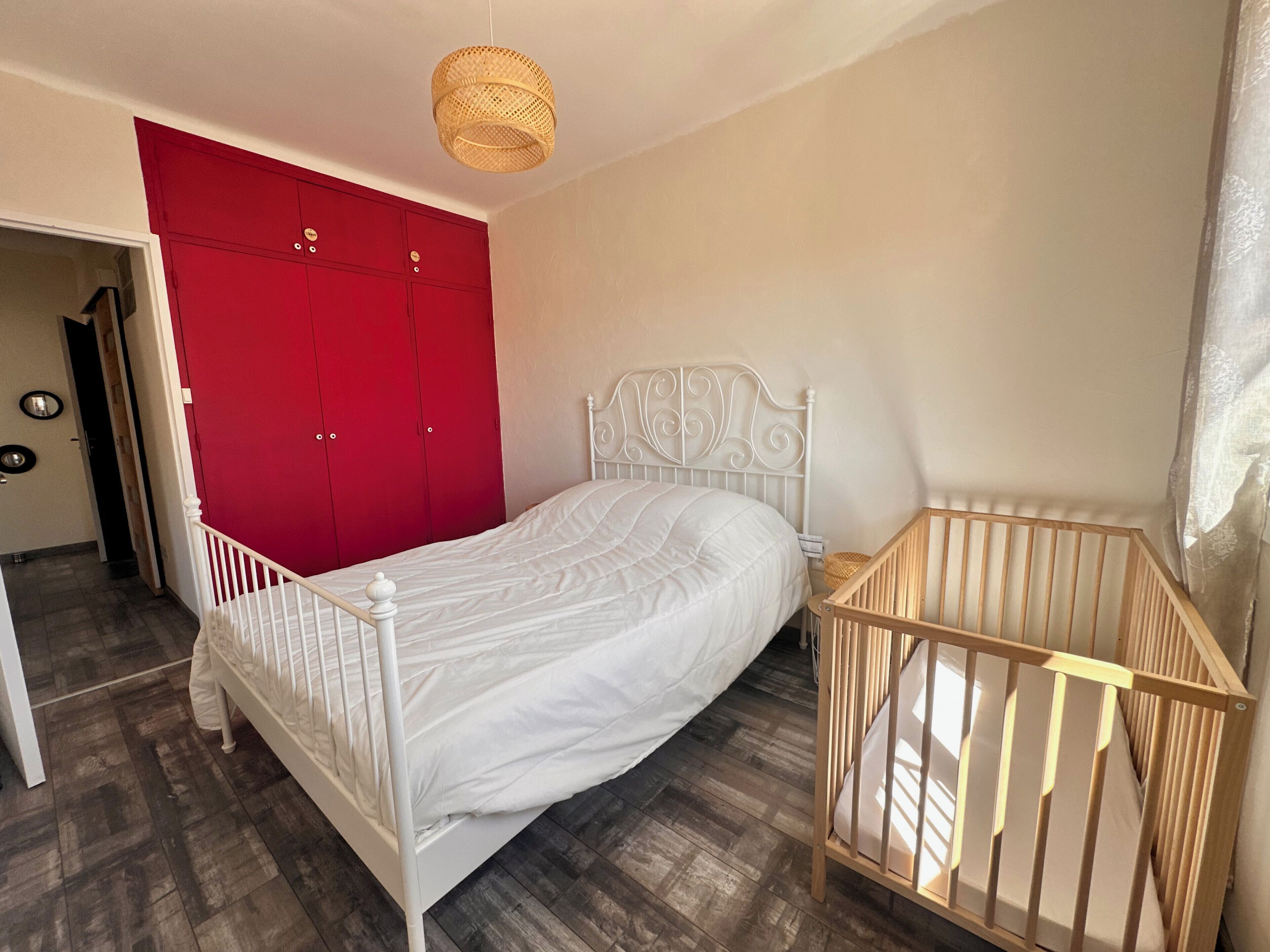 Un dormitorio con una cama blanca, un armario rojo y una cuna de madera.