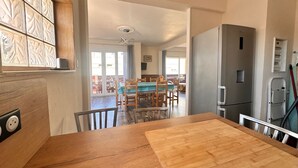 Une cuisine avec une table en bois, un réfrigérateur et un coin repas comprenant des chaises et une table.