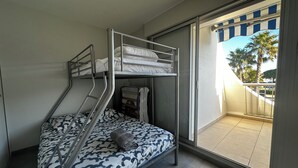Une chambre avec des lits superposés donnant sur un balcon et des palmiers.