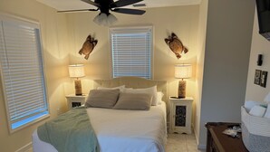 A bedroom with a bed, two nightstands with lamps, a ceiling fan, and two wall-mounted clocks. - Hibiscus House - Heated Pool (Big Pine Key)
