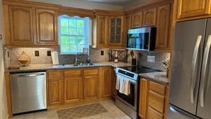 A kitchen with wooden cabinets, a stainless steel dishwasher, a microwave, an oven, and a refrigerator. - Hibiscus House - Heated Pool (Big Pine Key)