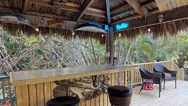 A wooden bar with two stools, surrounded by tropical plants and a thatched roof. - Hibiscus House - Heated Pool (Big Pine Key)