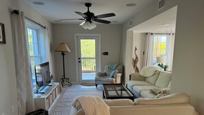 A living room with a sofa, a coffee table, a TV, a floor lamp, and a door leading to a balcony. - Hibiscus House - Heated Pool (Big Pine Key)