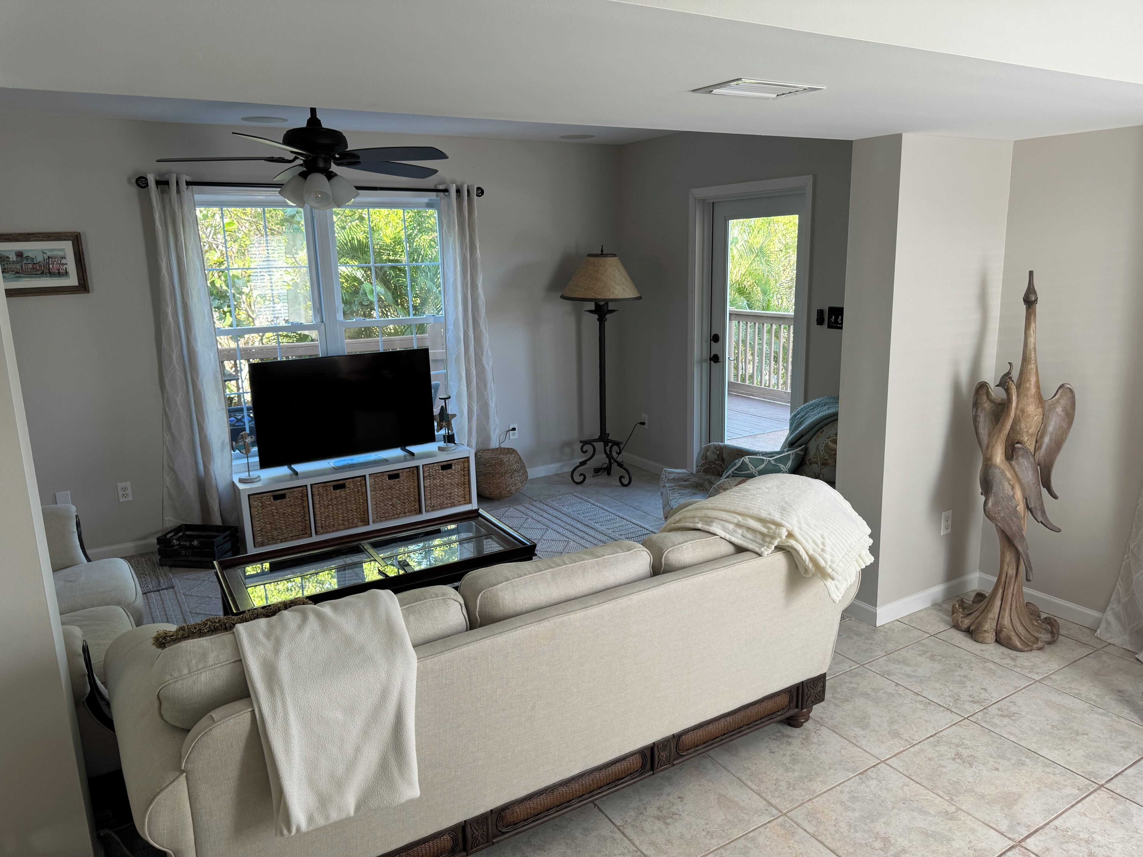 A living room with a sofa, a flat-screen TV, a ceiling fan, and a window with curtains.