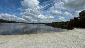 En sandstrand med ett lugnt sjölandskap och träd i bakgrunden.