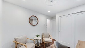Une pièce moderne avec deux chaises en bois, une petite table ornée d’une plante et un tapis à motifs.