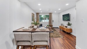 Un espace repas moderne avec une table en bois, deux chaises rembourrées, une console en bois et une grande fenêtre agrémentée de rideaux.