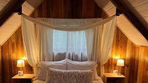 Ein gemütliches Schlafzimmer mit einem großen Bett, weißer Bettwäsche und einem Baldachin. Es gibt zwei Nachttische mit Lampen.