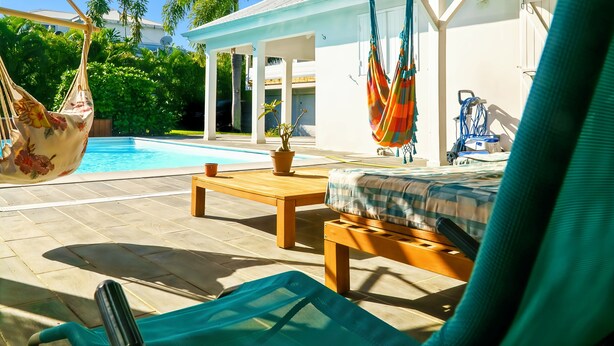 A poolside area with a hammock, lounge chairs, a wooden table, and a bed with a checkered bedspread. - Villa Gérika, privacy and elegance. Charming villa nestled in a private estate (Sainte-Anne)