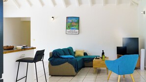 A living room with a sofa, a blue chair, a coffee table, a TV, and a painting on the wall. - Villa Gérika, privacy and elegance. Charming villa nestled in a private estate (Sainte-Anne)